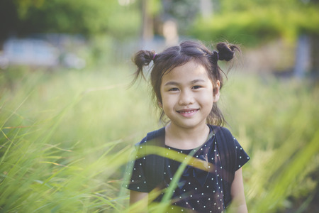 toothy smiling face of asian children standing in green leaves fieldの写真素材