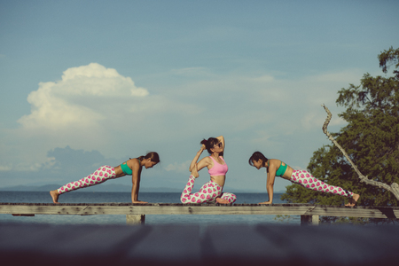 three asian woman playing yoga flow on beach pierの写真素材