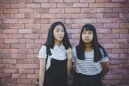 two asian teenager standing in front of red brick wall with surprising face