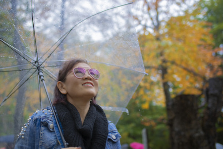 toothy smiling face of woman tourist with rain umbrella standing in autumn color leaves in hokkaido...