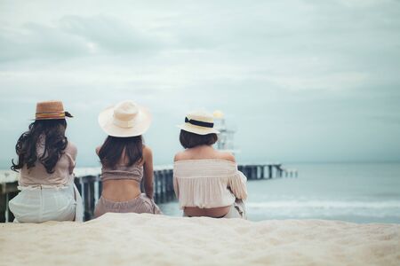 three woman wearing straw hat  sitting on vacation sea beach