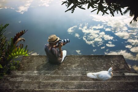 traveling man taking a photograph at old pier against beautiful blue sky reflection on water floorの写真素材