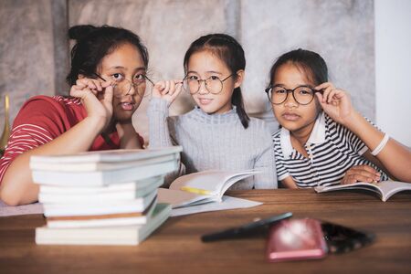 cheerful asian teenager wearing eye glasses with school book in home living roomの写真素材