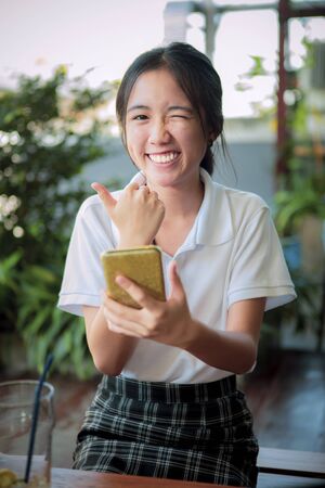 happiness asian teenager hand tumb sign okay and other hand holding smart phoneの写真素材