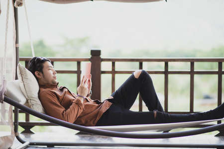 younger man relaxing by reading book on cradleの写真素材