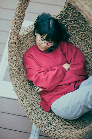asian teenager sleeping in bird nest swing at home terraceの写真素材