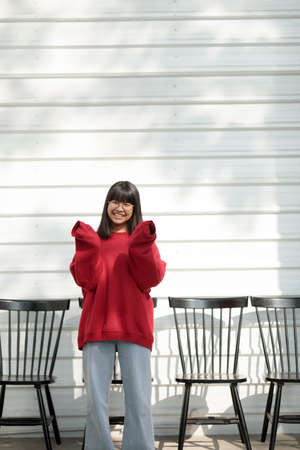 asian teenager wearing red sweater standing against white wall