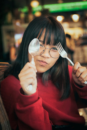 funny face of asian teenager raise fork and spoon in dinning room