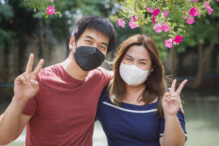 asian couple wearing protection face mask hand sign victory standing outdoorの写真素材