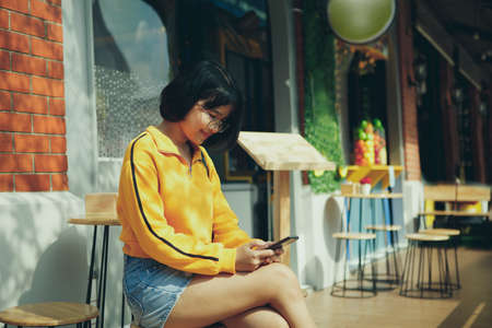 asian teenager checking message on mobilephone at city street cafeの写真素材