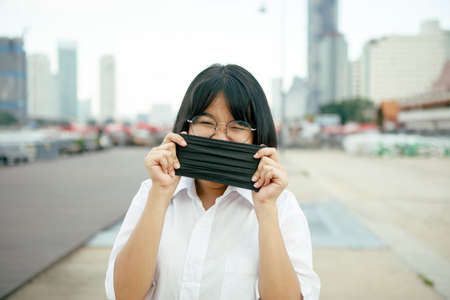 asian teenager with protection face mask in hand standing outdoorの写真素材