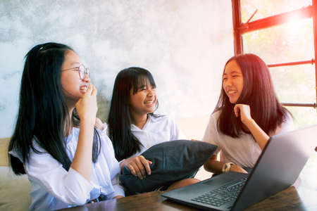 three asian teenager laughing with happiness face while working on aptop in living roomの写真素材