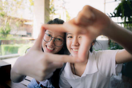 two asian teenager hand sign as photo frame with happiness face behindの写真素材
