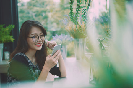 beautiful asian younger woman reading message in smart phone and smiling with happiness faceの写真素材
