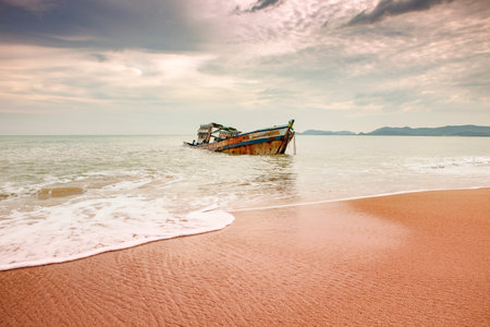 seascape of wreck boat on sand beach with cloudy sky in tropical region seasonの写真素材