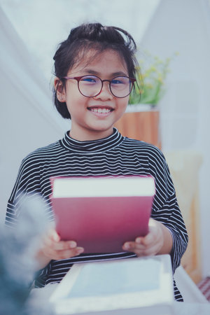 asian girl holding big school book in hand and toothy smiling with happinessの写真素材
