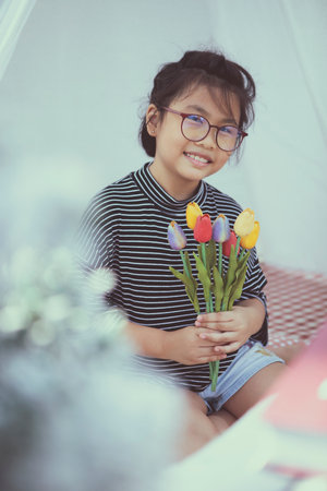 asian kid holding artificial of tulip flower in hand toothy smiling with happinessの写真素材