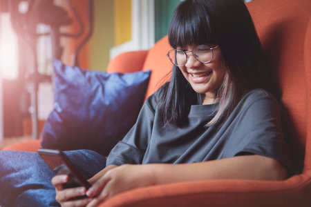 asian teenager reading message in smartphone with happiness face at home living roomの写真素材