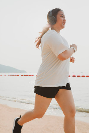 chubby woman wearing sport wear and haedphone running on sea beach with happinessの写真素材