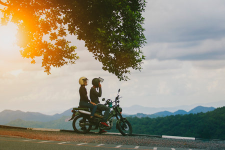 couples wearing safety helmet sitting on small enduro motorcycle against beautiful natural mountain scene at khaoyai national park thailandの写真素材