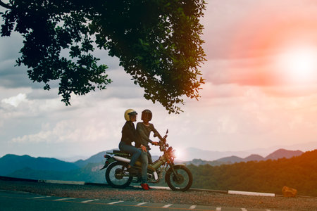 couples wearing safety helmet sitting on small enduro motorcycle against beautiful natural mountain scene at khaoyai national park thailandの写真素材