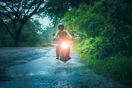 man riding small endurom motorcycle crossing shallow creek among rain falling at forestの写真素材