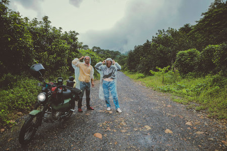 couples of asian biker wearing plastic rain clothes standing beside small enduro motorcycle on country trackの写真素材