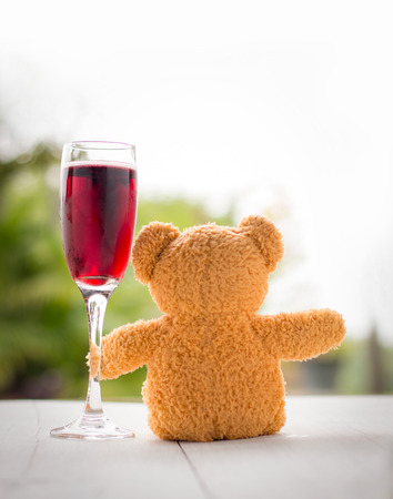 valentine concept. teddy bear with red wine glass over bokeh green garden background.の写真素材