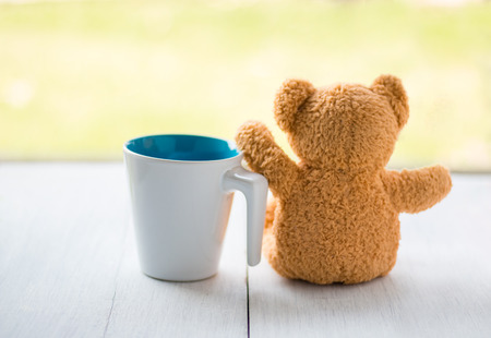 relax concept. teddy bear with white coffee mug over bokeh green garden background.の写真素材