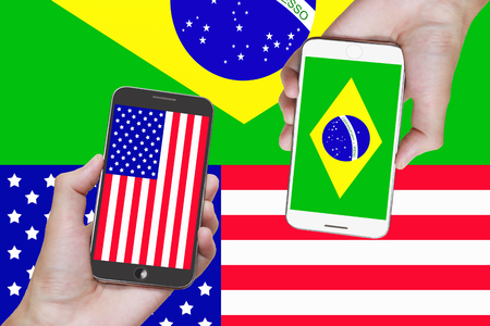 Man hand holding mobile smart phone with United States flag and brazil on the white backgroundの写真素材