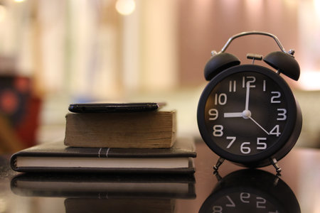Alarm clock and books on a black reflective surface. Selective focus.の写真素材