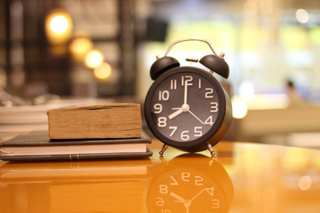 Alarm clock and book on the table in coffee shop blur backgroundの写真素材