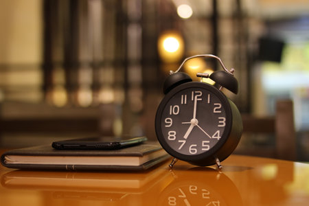 Alarm clock and notebook on the table in coffee shop background.の写真素材