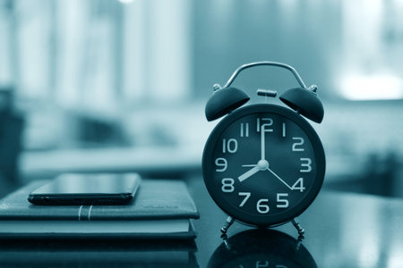 Alarm clock and notebook on table in office, black and white toneの写真素材