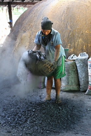 Nakhon Si Thammarat, Thailand - June 12, 2012 : A worker sifts through charcoal pieces. Separating small pieces before packing into a bag for sell.のeditorial素材