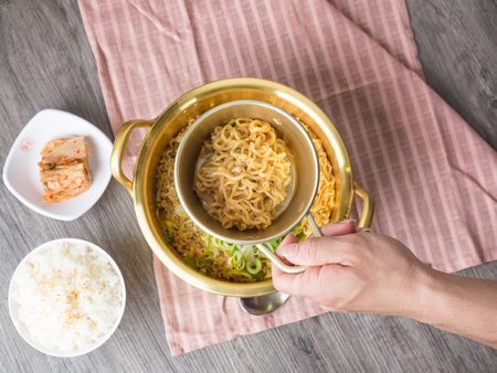 Hot korean instant noodle in big pot serve with rice and kimchi on wood background