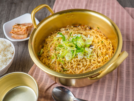 Hot korean instant noodle in big pot serve with rice and kimchi on wood backgroundの写真素材