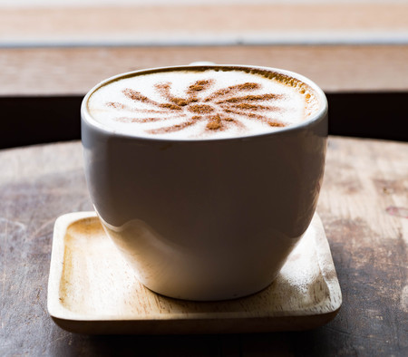 Late art coffee in white ceramic mug on wood table next to the window for relax timeの写真素材