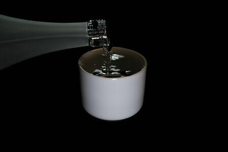 Tokyo,Japan-November 25, 2019: Pouring Sake into a Pottery Sake Cup on Black Backgroundの写真素材