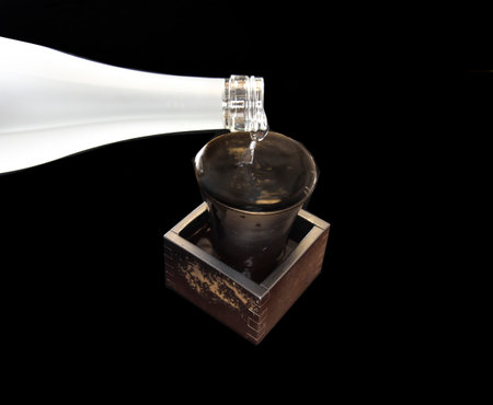 Pouring sake from bottle into Bizen-yaki or Bizen ware cup and square box on black backgroundの写真素材