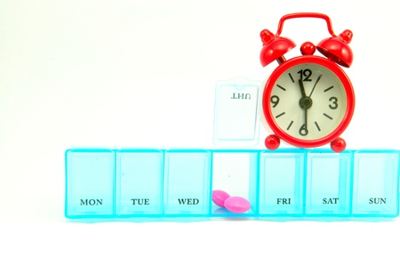 Daily pill box and red clock on white blackground show medicine time conceptの写真素材