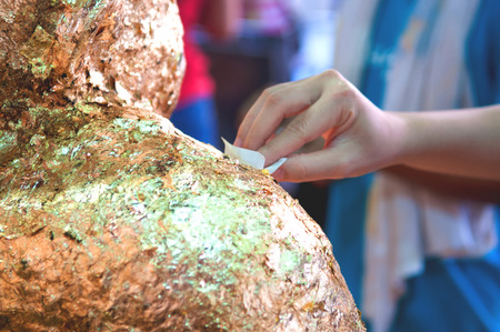Closed up hand placing gold leaf on buddhaの写真素材