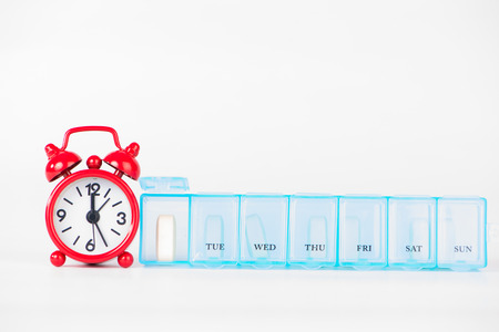 Weekly pill box and red clock show medicine timeの写真素材