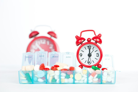 Red alarm clock and medicine in weekly pill boxの写真素材