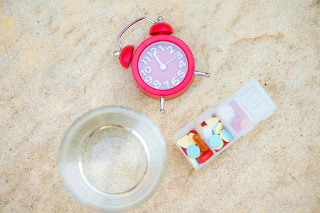 Red alarm clock,daily pill box and glass of water show medicine timeの写真素材