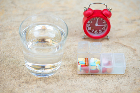 Red alarm clock,daily pill box and glass of water show medicine time