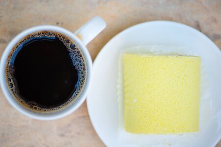 Black coffee and Sponge cake cream roll on white dish show bakery backgroundの写真素材