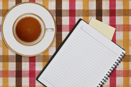 notebook and cup of coffee on picnic tableclothの写真素材
