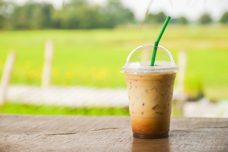 plastic glass of iced coffee on wooden balcony with green nature backgroundの写真素材