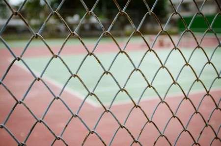 Wire fence with tennis court on background